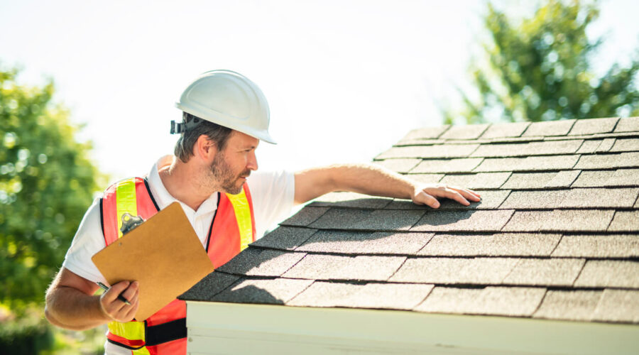 Man with hard hat standing on steps inspecting house roof